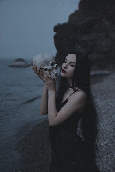 a woman with long hair holding a skull in her hand near the water and rocks