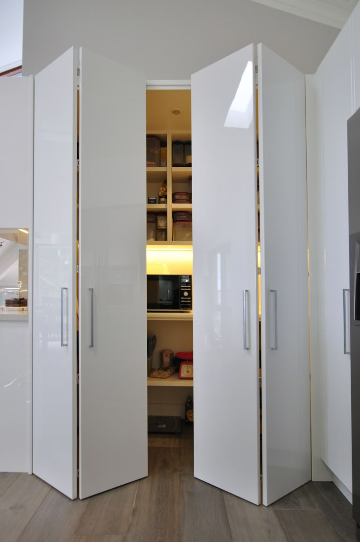 two tall white cabinets in a room with wood floors and walls, one is open to the other side