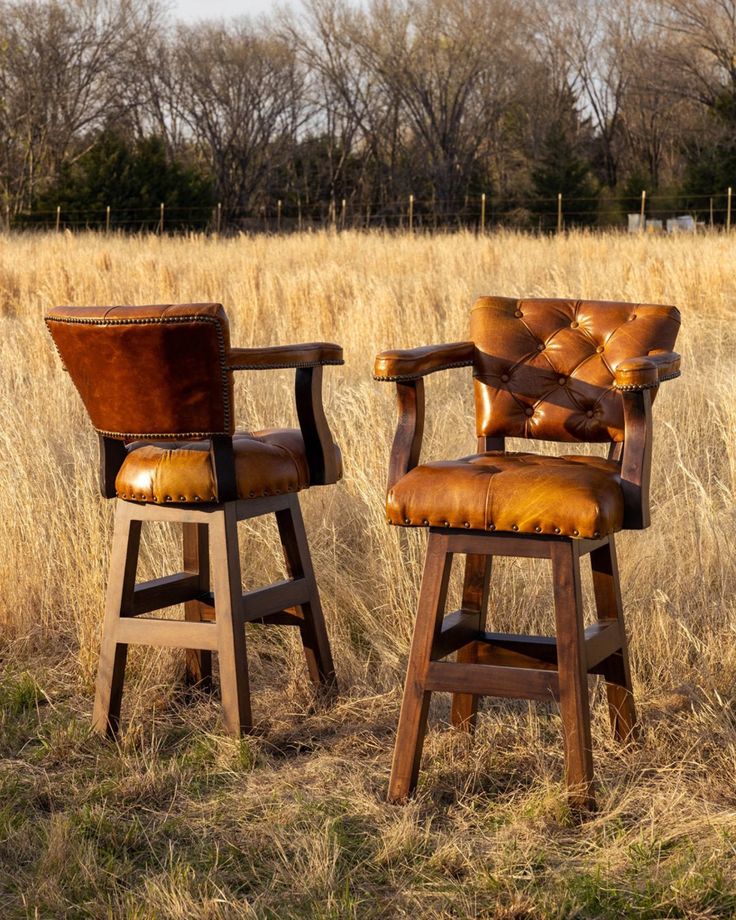 two brown leather chairs sitting on top of a grass covered field next to each other