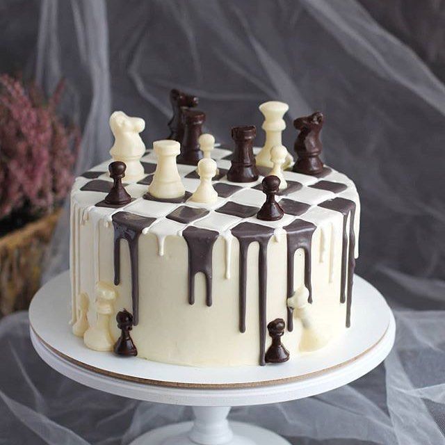 a cake decorated with chess pieces and chocolate glazes on a white pedestal stand