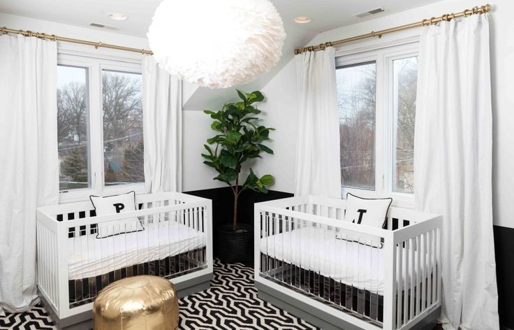 two white cribs in a black and white nursery with a gold footstool