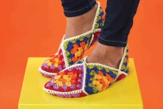 a woman's feet wearing colorful crochet shoes on top of a yellow platform