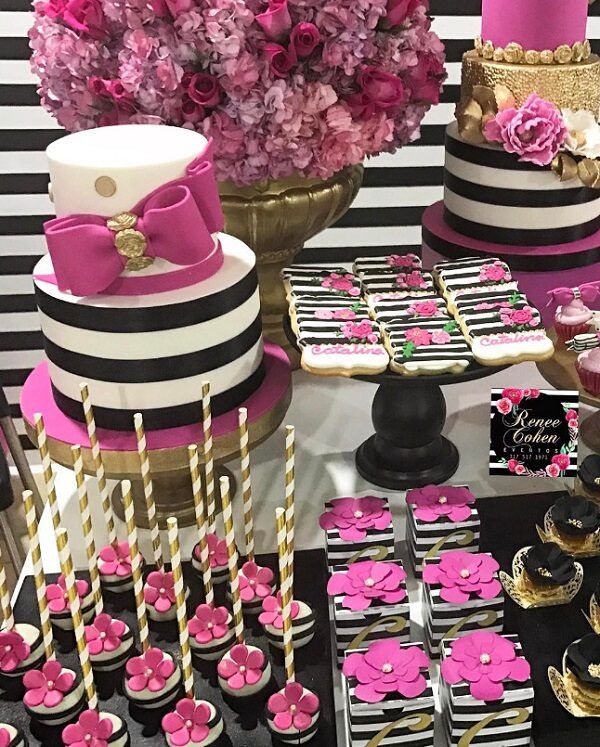 a table topped with lots of cakes and cupcakes covered in frosting next to pink flowers