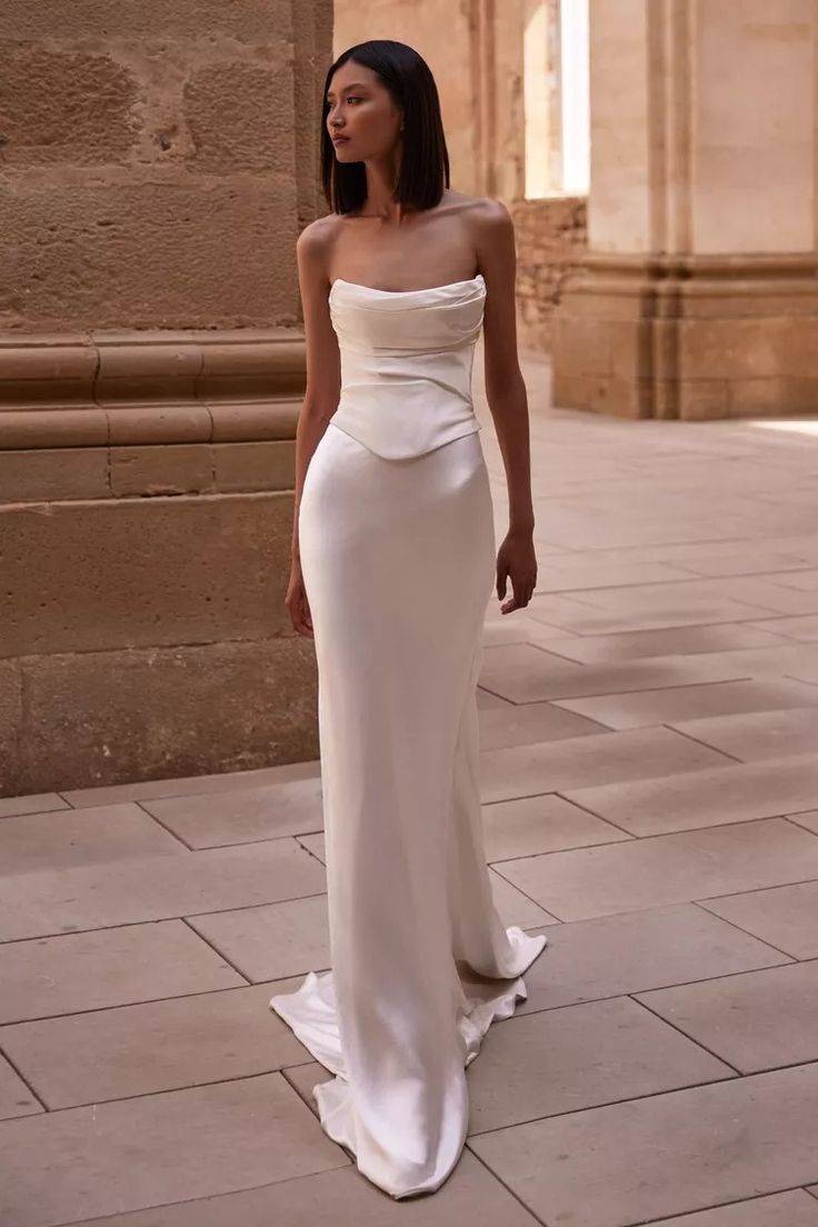 a woman in a white dress is standing on the sidewalk and looking off into the distance