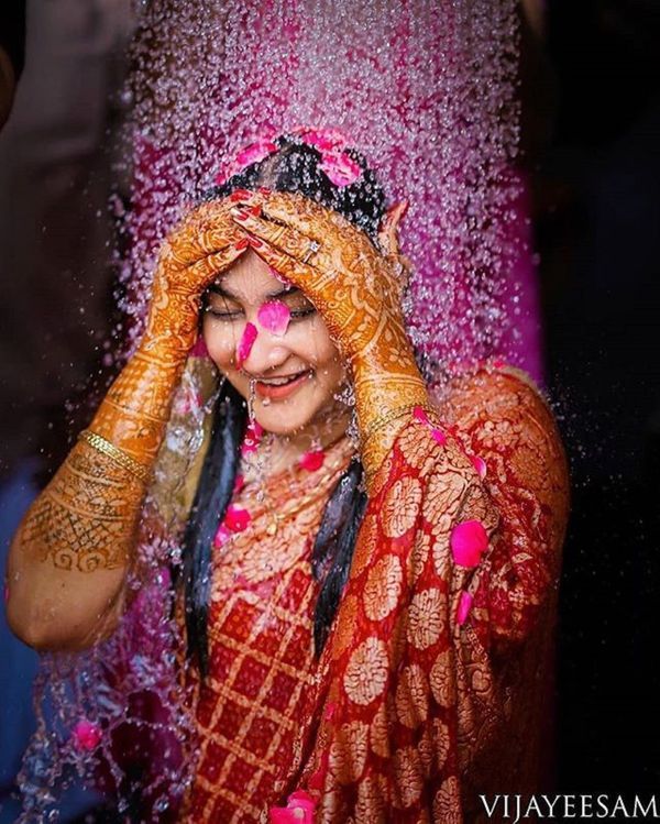 a woman covered in pink and orange powder throwing water on her face with her hands