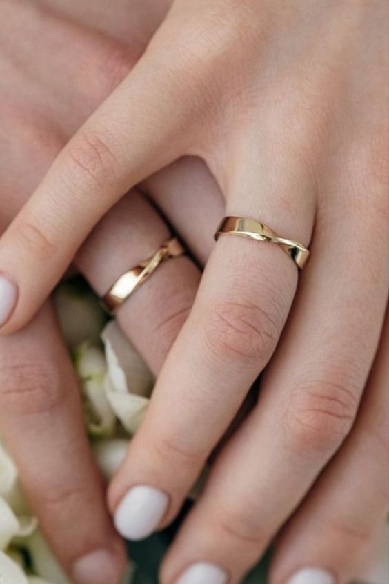 two people holding hands with wedding rings on top of each other and flowers in the background