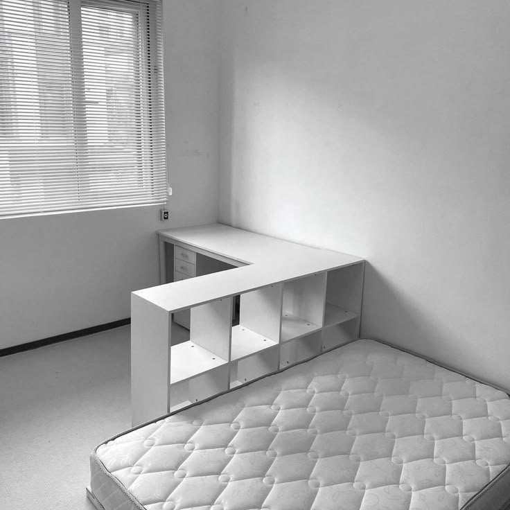 an empty room with a bed, desk and shelves on the wall next to it