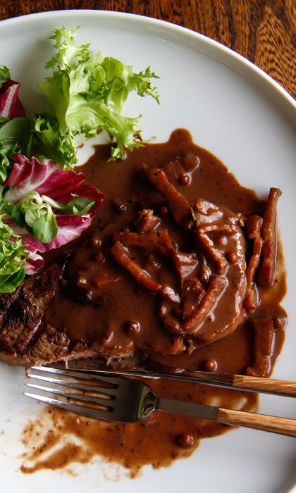 a white plate topped with meat covered in gravy and veggies next to a fork