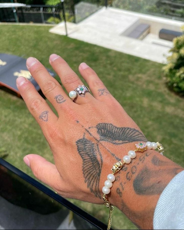 a person's hand with tattoos and pearls on it