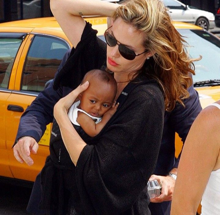 a woman holding a baby in her arms while walking down the street with other people