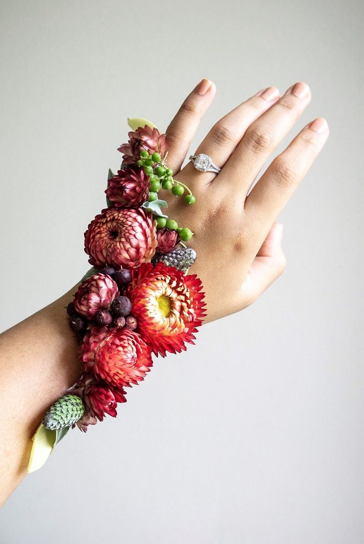 a woman's hand wearing a bracelet made out of flowers and berries on it