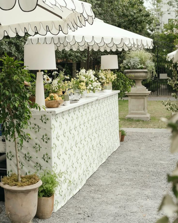 an outdoor bar with white umbrellas and potted plants on the table in front of it