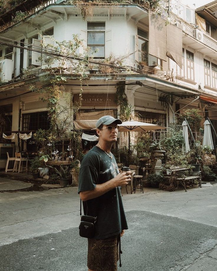 a man standing in front of a building holding a cell phone and wearing a hat