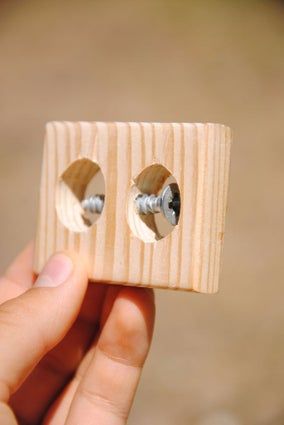 a hand holding a piece of wood with two screws in the middle of it