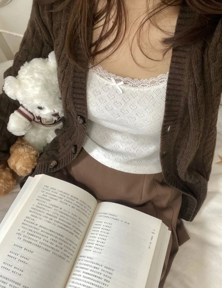 a woman sitting on a bed with an open book and teddy bear in her lap