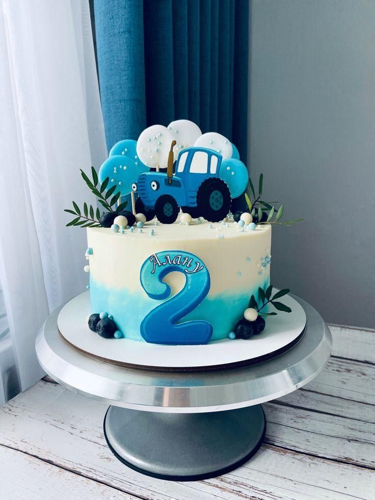 a blue and white cake with two cars on it sitting on a table next to a window