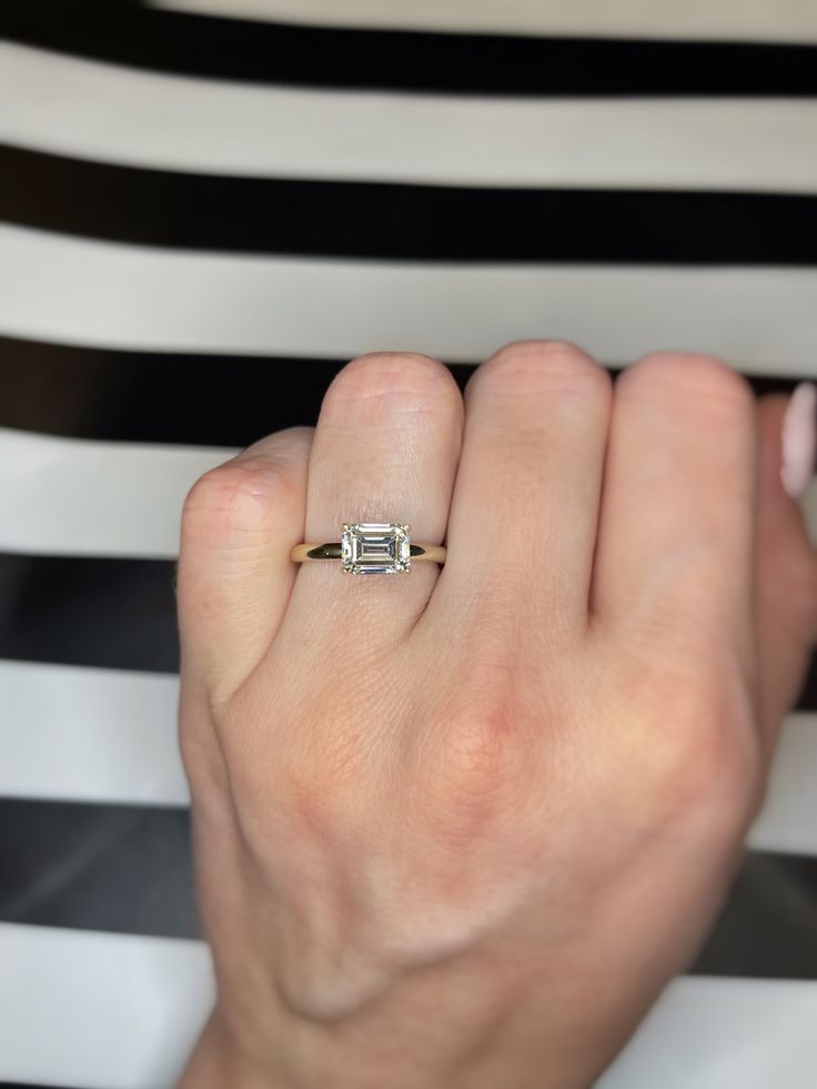 a woman's hand with a diamond ring on her left finger, and a black and white striped chair in the background