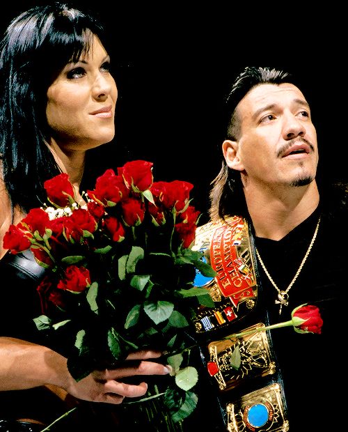 a man and woman standing next to each other holding roses