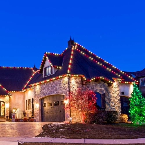 a house with christmas lights on the roof and trees around it's front door