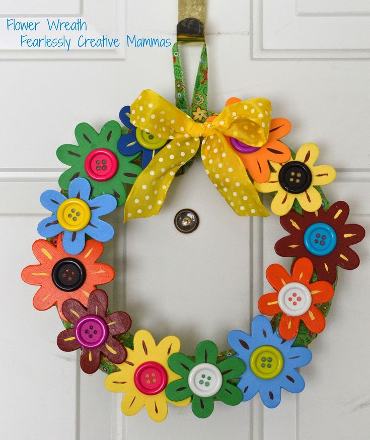 a colorful flower wreath is hanging on the front door with a button and ribbon attached to it