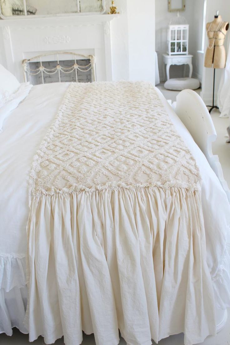 a white bed with ruffled bedspread and pillows