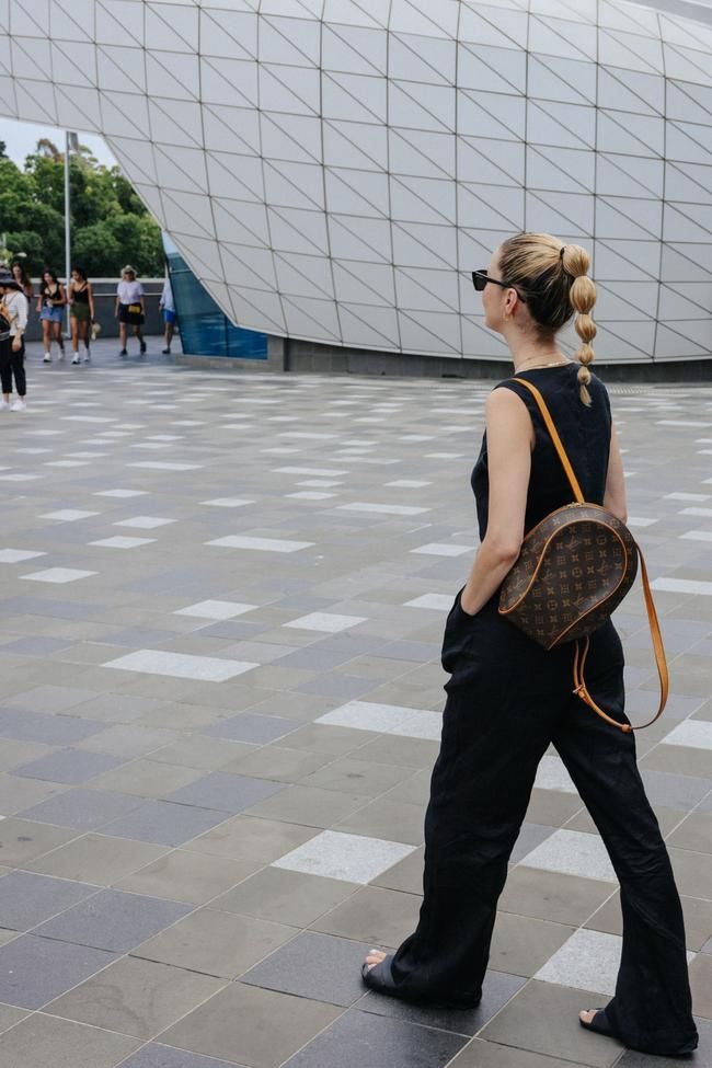 a woman walking down the street carrying a louis vuitton bag in her hand