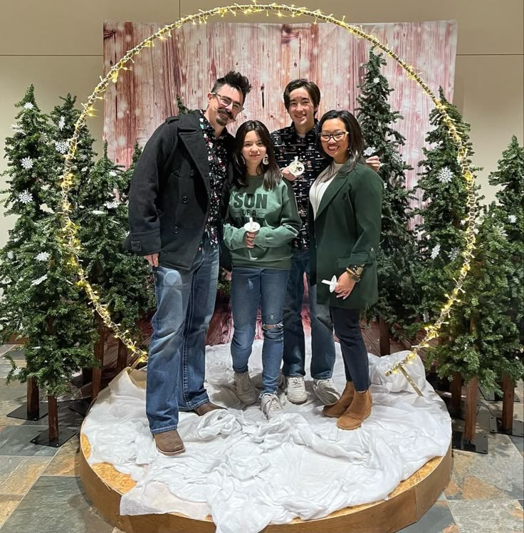 four people posing for a photo in front of christmas trees