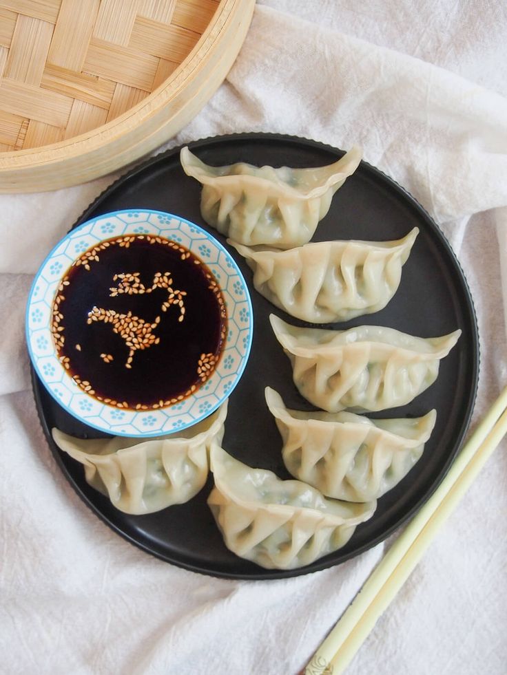 some dumplings are on a black plate with chopsticks