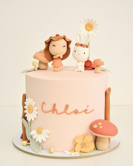 a pink cake with two small figurines sitting on top of it and flowers