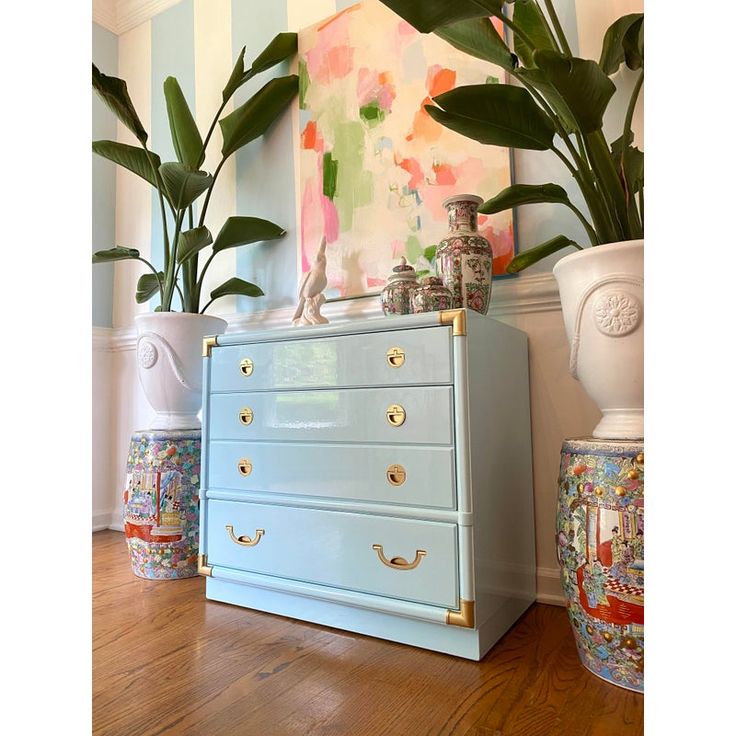 a blue dresser sitting next to two potted plants on top of a wooden floor