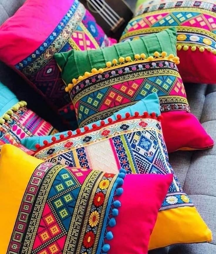 many colorful pillows are on a couch with some tassels and beads around the edges