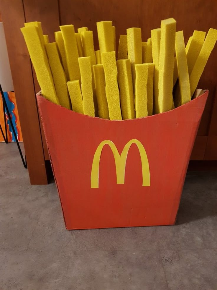 a red box filled with yellow fries sitting on top of a carpeted floor next to a wooden cabinet