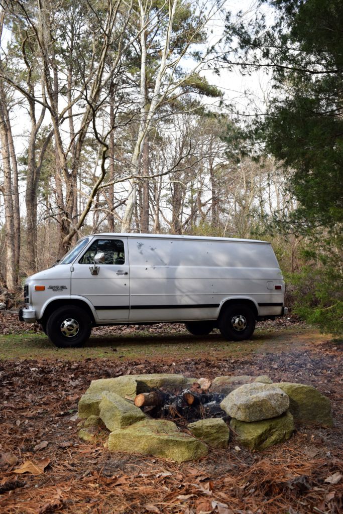 a van parked in the woods next to a fire pit with rocks and trees around it