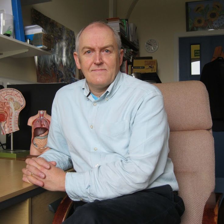 an older man sitting at a desk with his arms crossed and looking into the camera