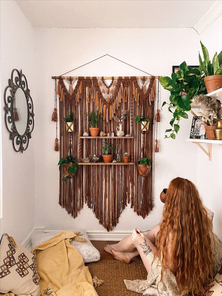 a woman is sitting on the floor in front of a wall hanging with potted plants