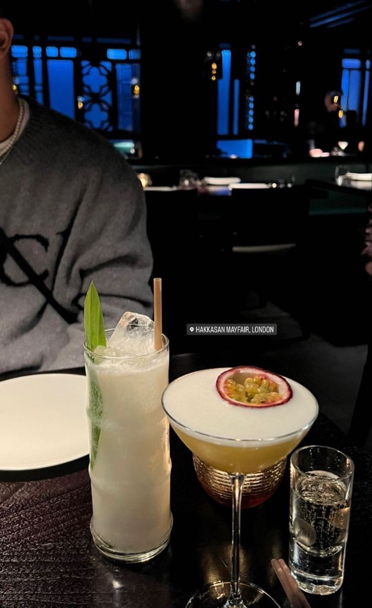 a man sitting at a table with two drinks in front of him and another drink next to him