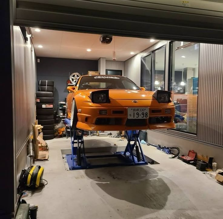 an orange car is on a lift in a garage with other cars and tools around it