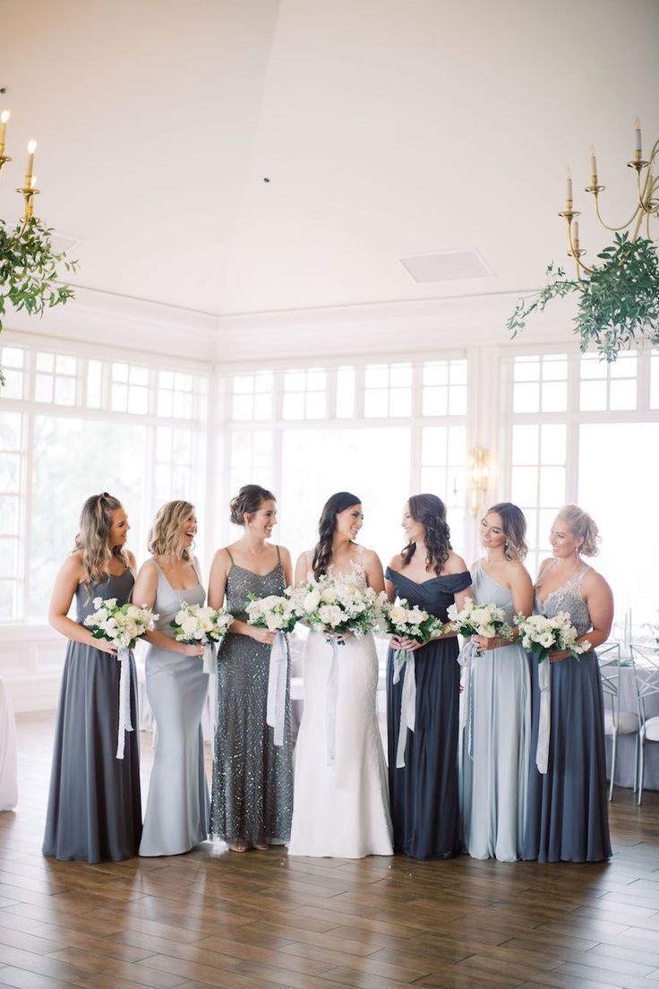 a group of women standing next to each other in front of a window holding bouquets