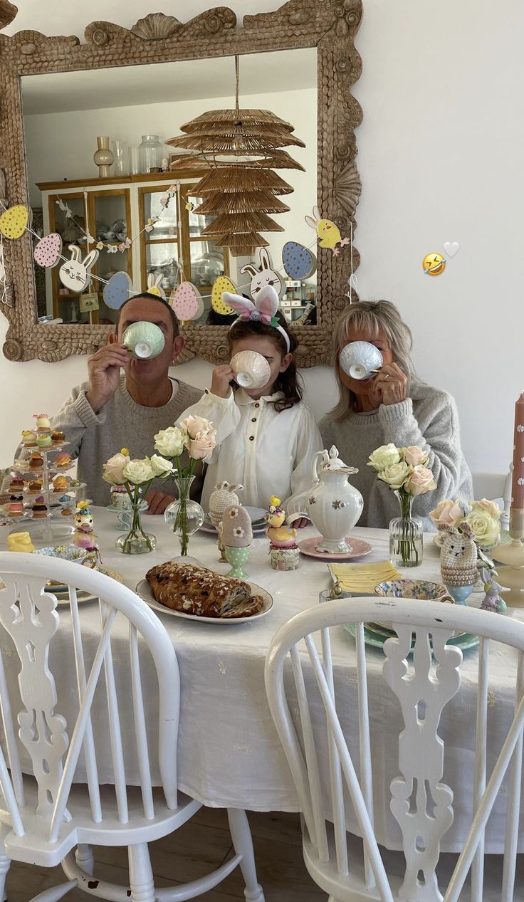 three people sitting at a table with plates and cups in front of them, wearing masks