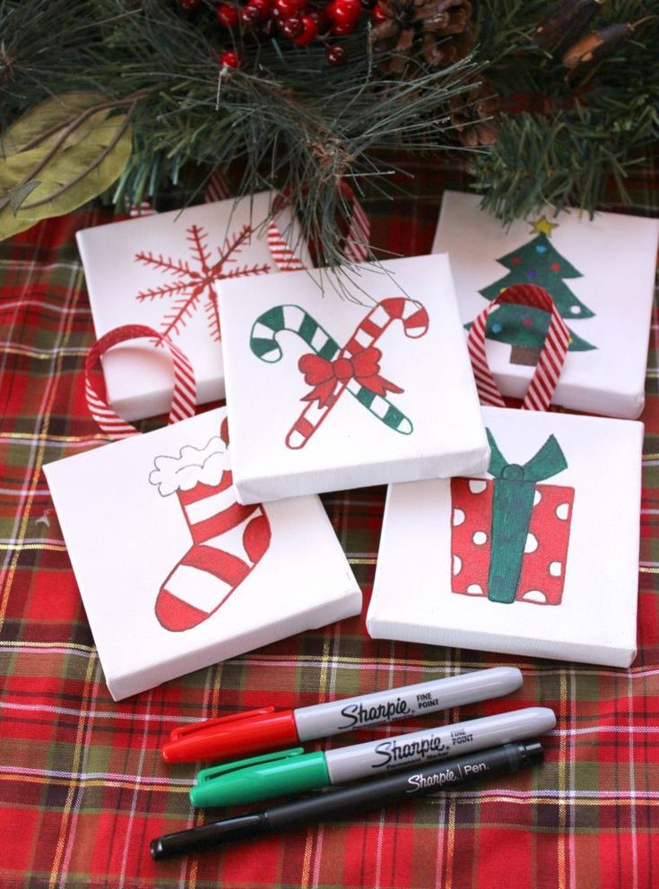 four christmas cards and markers on a plaid tablecloth next to a pine tree with candy canes