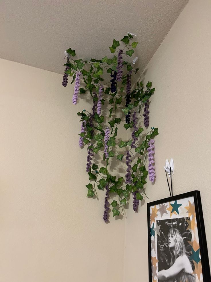 purple flowers are hanging from the ceiling above a framed photo and an art piece is hung on the wall