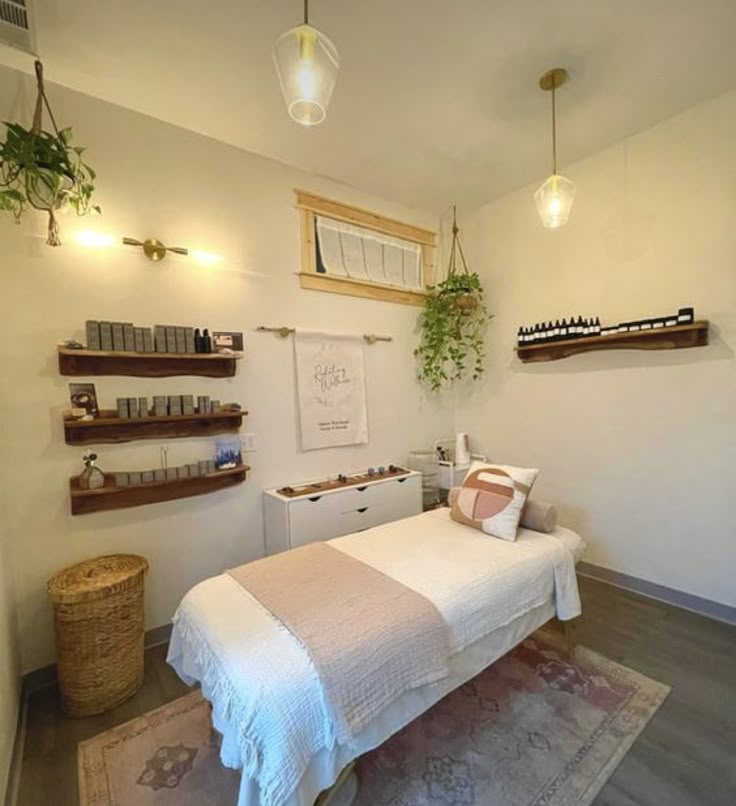 a white bed sitting in a bedroom on top of a wooden floor next to a shelf filled with bottles