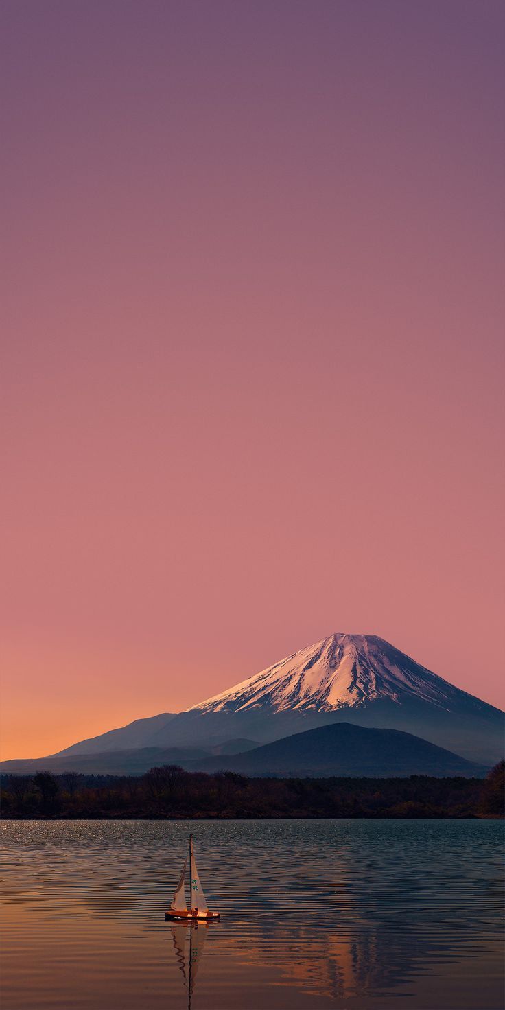 a boat floating on top of a body of water under a snow covered mountain in the distance