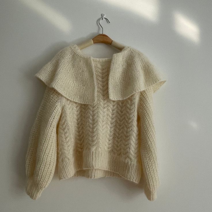 a white sweater hanging on a wooden hanger