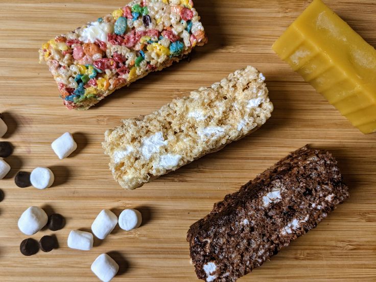 four different types of candy bars on a wooden table with marshmallows and chocolate chips