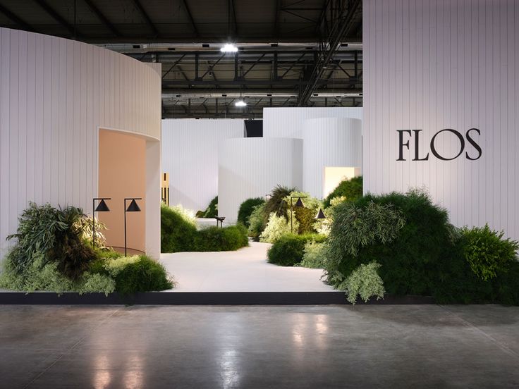 the entrance to flos is surrounded by lush green plants and trees in front of a white wall