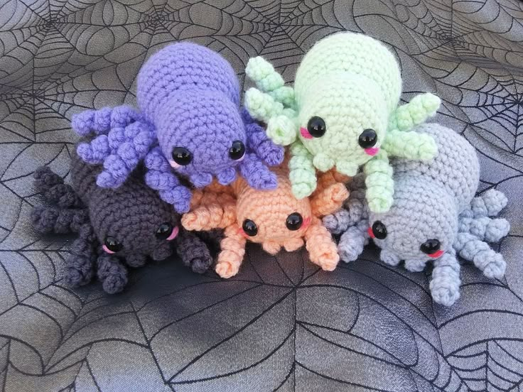 four crocheted stuffed animals sitting next to each other on a bed with spider webs