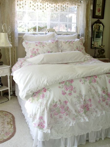 a white bed with pink flowers on it in a bedroom next to a window and rug