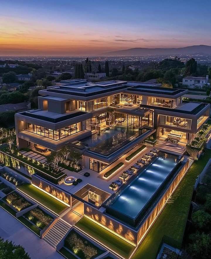 an aerial view of a large house at dusk with the lights on and swimming pool in the foreground