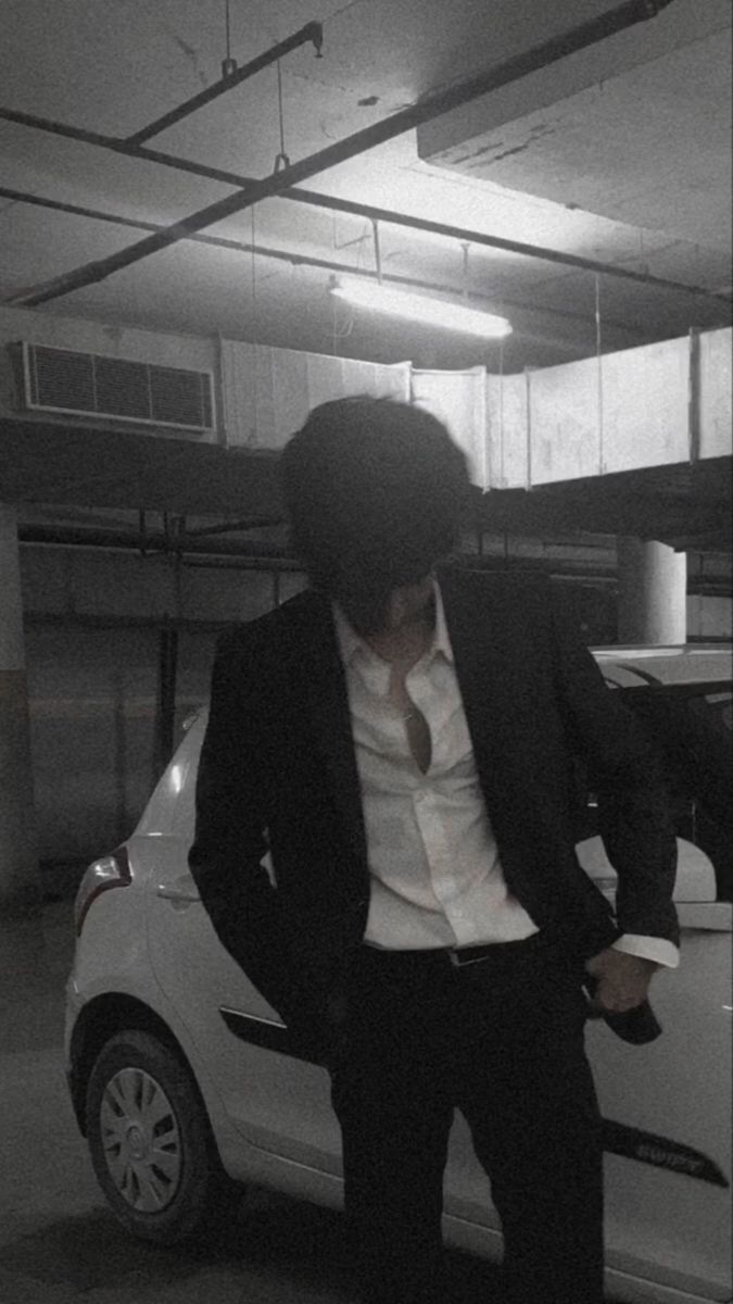 a man standing next to a white car in a parking garage wearing a suit and tie